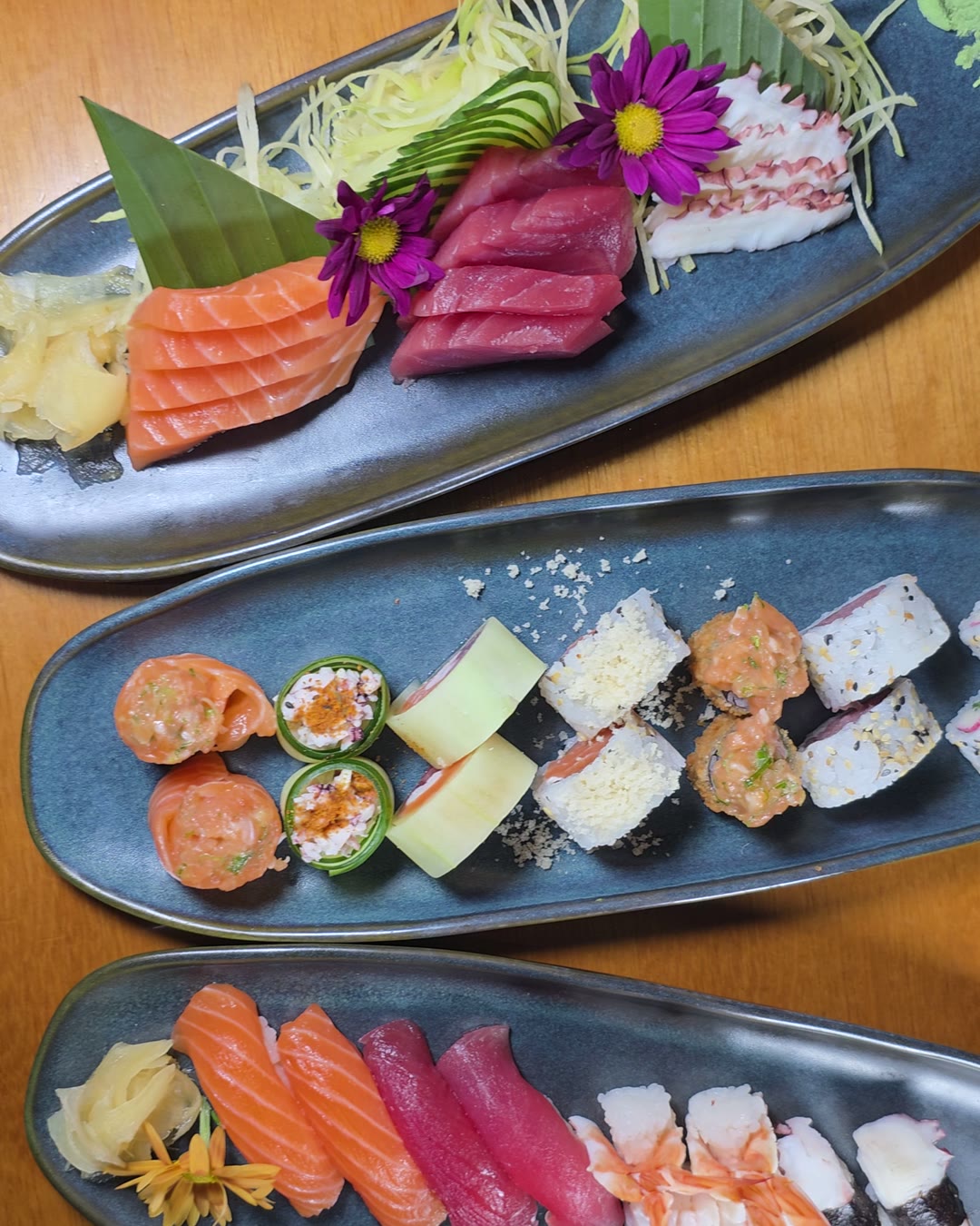 Três travessas com sashimi, uramaki e niguiri