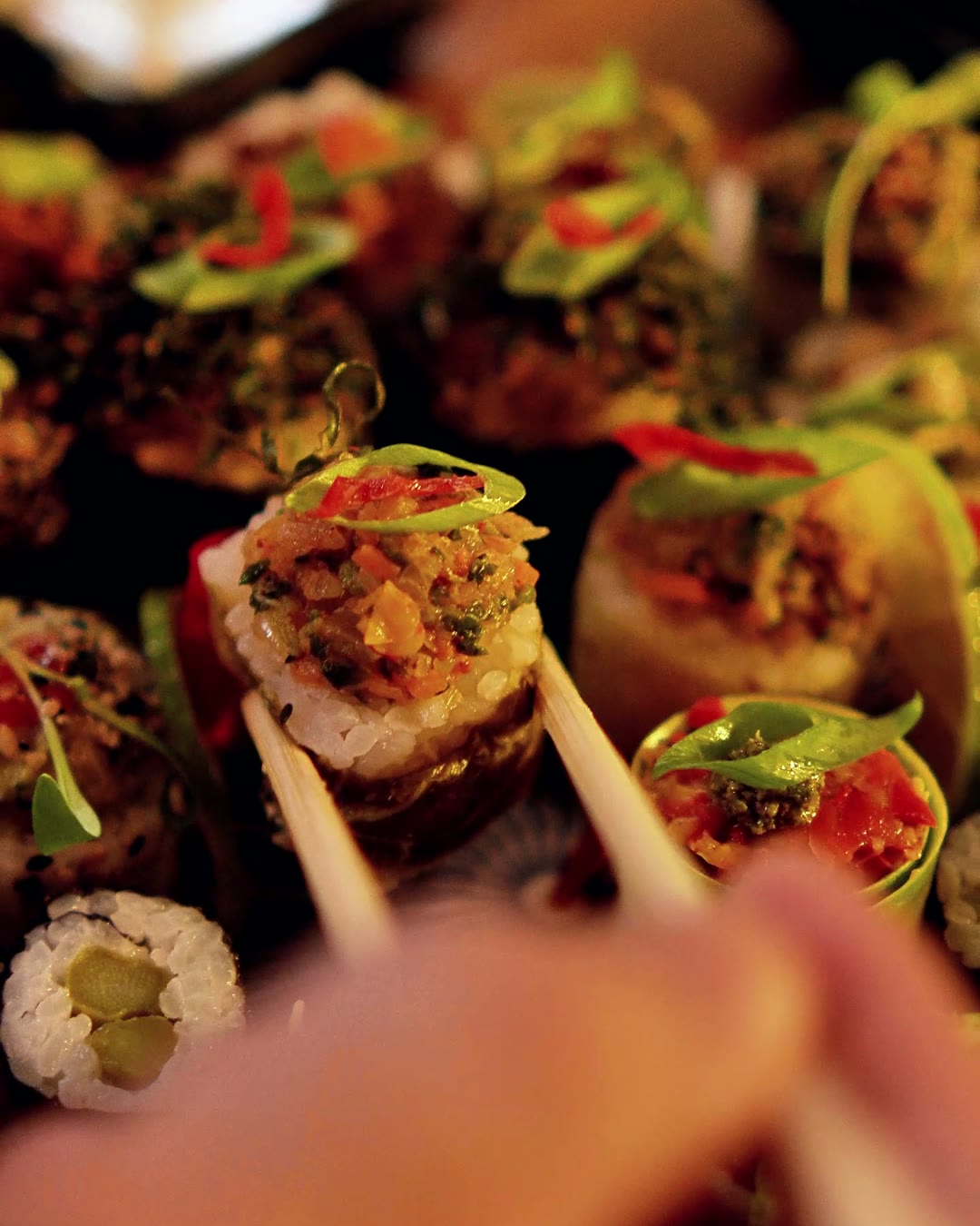 Sushi vegano levantado com hashi entre outras peças